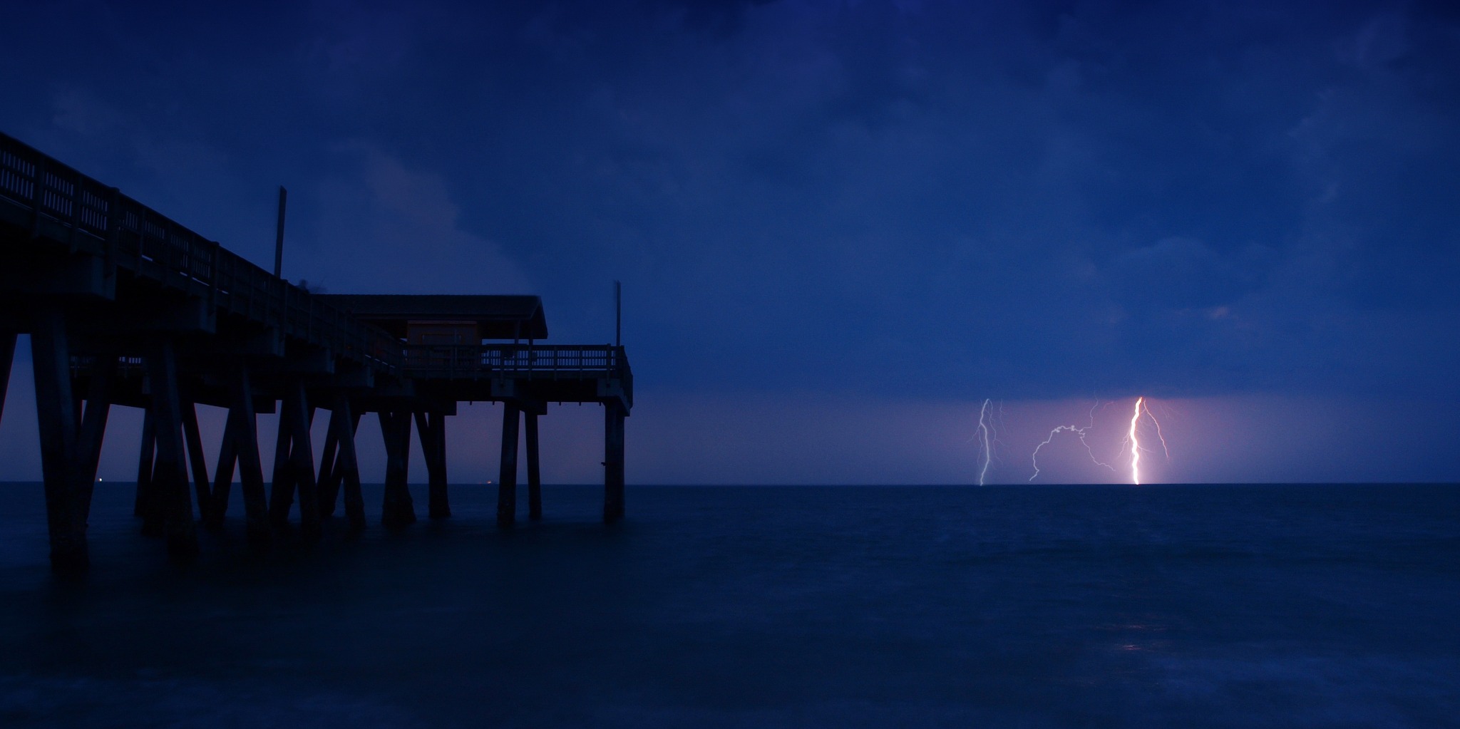 Lightning over the ocean beside a pier